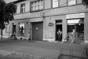 Czempiń, Rynek. Godz. 12:51. Od prawej stoją: p. Irena Karczmarek, sprzedawczyni w sklepie spożywczym, p. Maria Guz, mieszkanka środkowego domu, z lewej strony siedzi na schodach p. Kamil Biernacki, który uczy się historii.