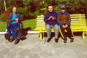 Fot. Kazimiera Czaińska. Zdjęcie przedstawia mieszkańców Domu Pomocy Społecznej w Jarogniewicach wygrzewających się w pierwszych promieniach czerwcowego słońca. Zdjęcie wykonano przy klombie, naprzeciwko budynku Betania.