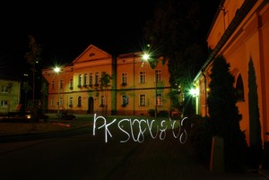 08.08.08 kilka minut po godzinie dwunastej w nocy. Plac Niezłomnych w Kościanie, zdjęcie wykonane od strony ulicy Sądowej. Przedstawiony jest Sąd rejonowy oraz kościół pod  wezwaniem Pana Jezusa. Długi czas naświetlania, silne punktowe źródło światła oraz zwinne ręce pozwoliły na wykonanie napisu który charakteryzuje tematykę projektu.   Fot. Krzysztof Szydłowski