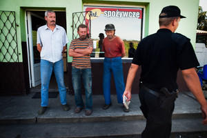 Nowe Oborzyska godz. 13:50. St. sierż. Tomasz Bajstok idzie wyjaśnić okoliczności zgłoszenia o psach, które miały zaatakować rowerzystkę w rejonie sklepu.  Jak widać wszyscy patrzą policji na ręce.